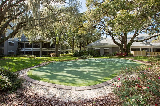 A serene garden scene featuring a well-maintained putting green surrounded by lush trees and landscaping.