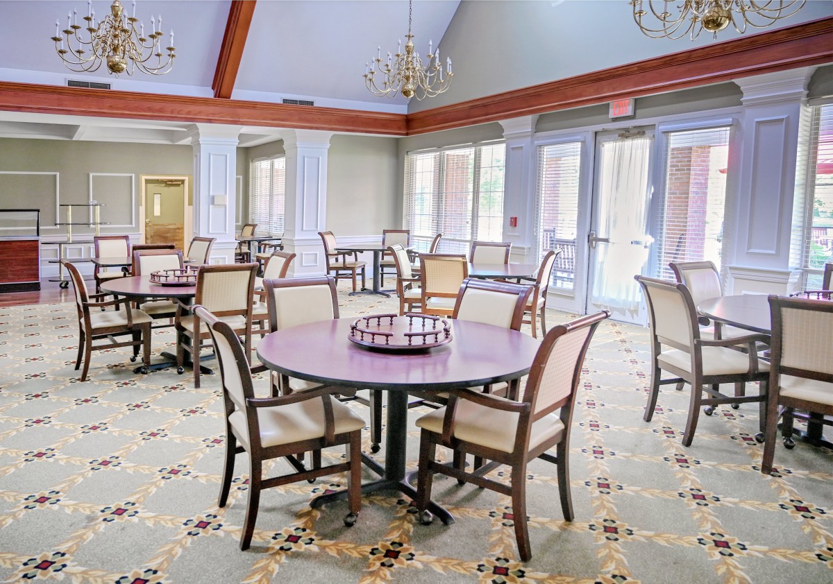 A spacious dining room with neatly arranged tables and chairs, illuminated by chandeliers.