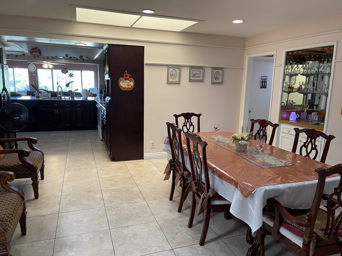 A spacious dining room with a view into the kitchen, featuring a long table and wooden chairs.