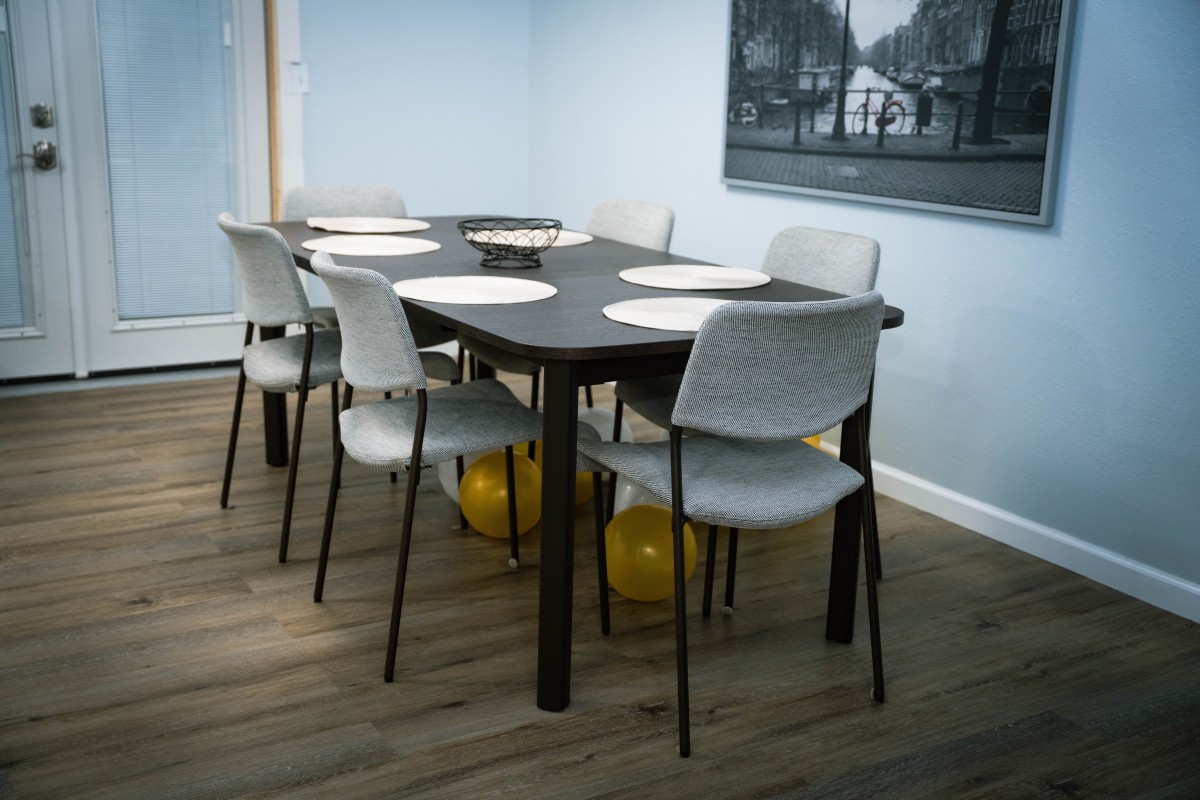 A dining room with a modern table set for six, featuring white chairs and balloons underneath.