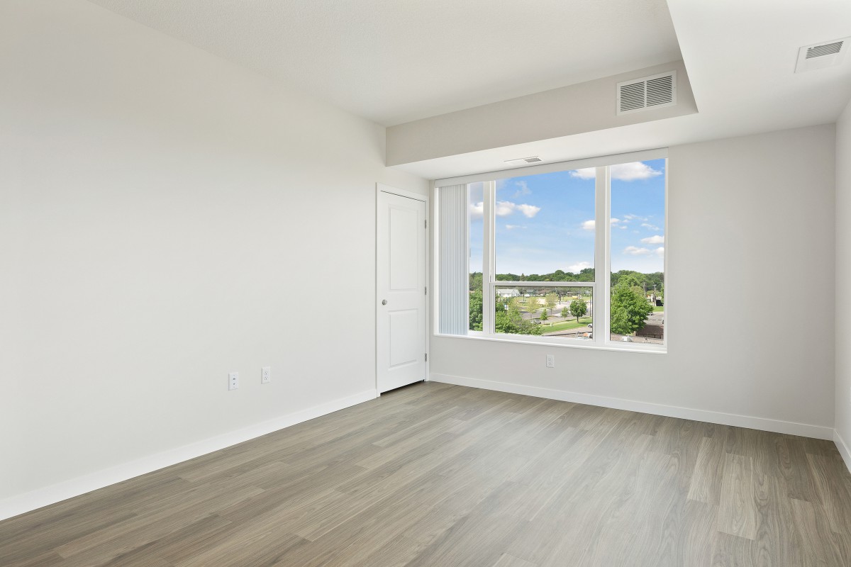 A bright, empty room with hardwood floors and a large window offering a scenic view.