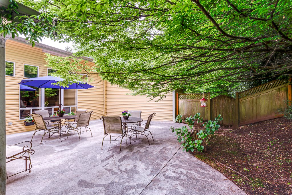 A cozy patio area with outdoor seating under the shade of lush trees.