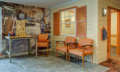 A cozy waiting room with orange chairs and a decorative wall.