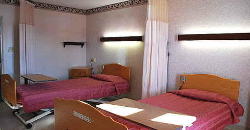 A simple hotel room featuring two twin beds with pink bedding and soft lighting.
