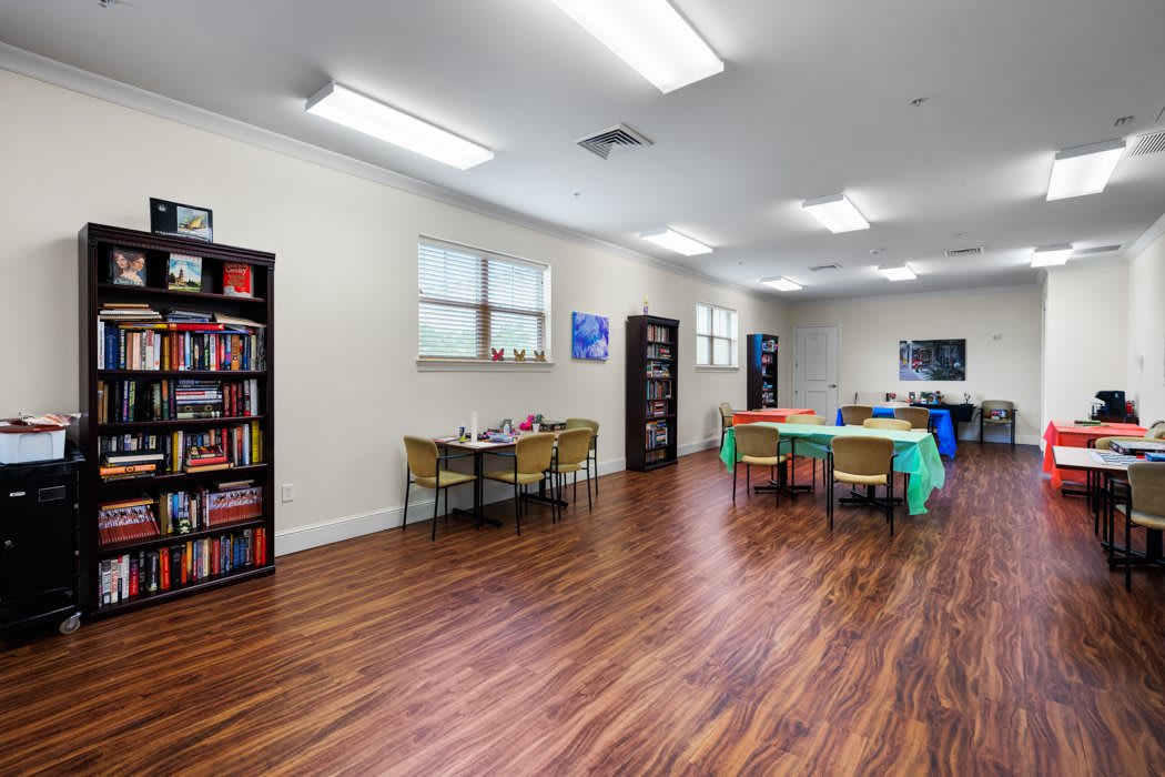 A classroom with tables, chairs, and bookshelves on a hardwood floor.