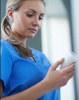 A healthcare professional in a blue uniform examines a bottle.