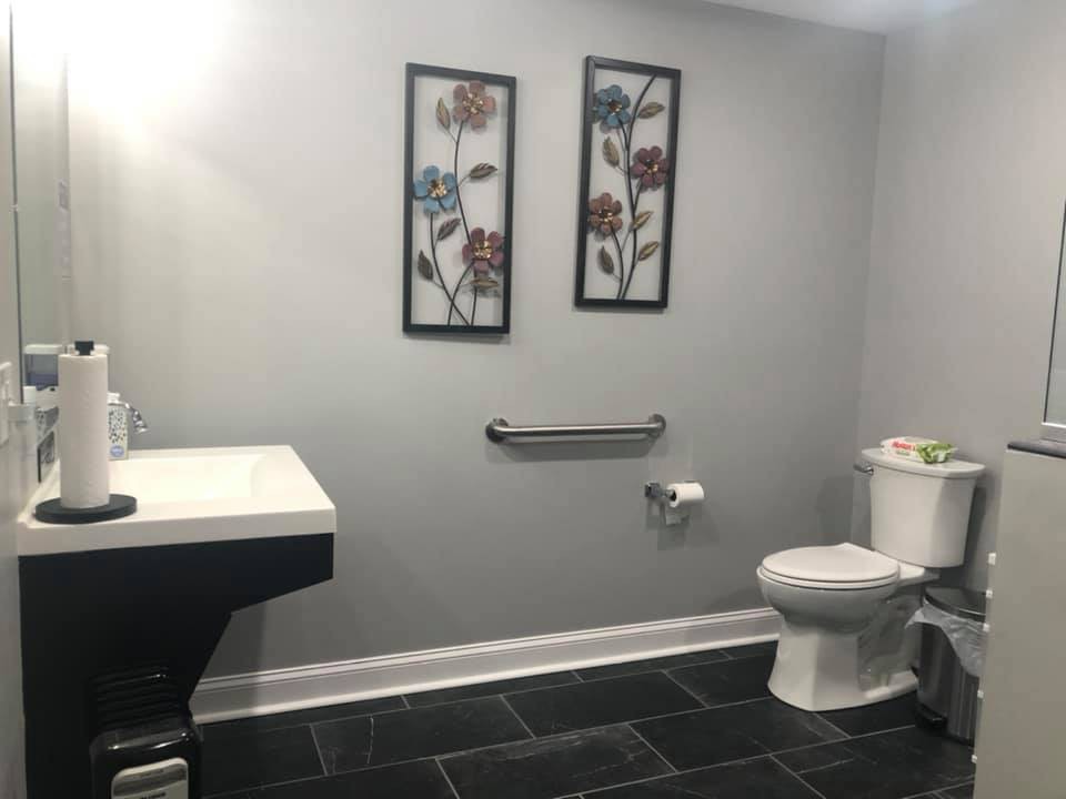 A modern bathroom with grey walls, featuring floral artwork, a toilet, and a sleek sink.