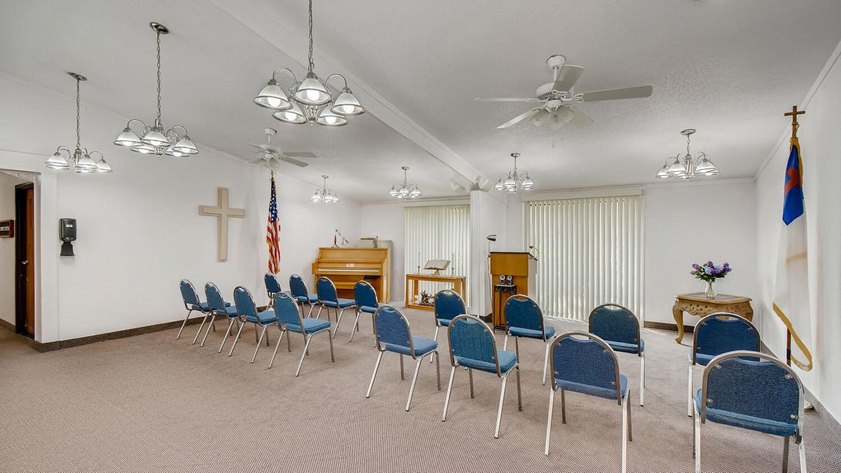 An interior view of a chapel with rows of blue chairs, a piano, a podium, and religious symbols.