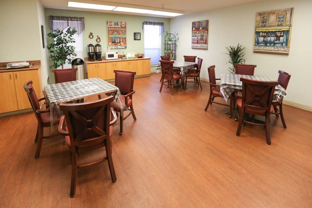 A cozy dining area with wooden floors and neatly arranged tables and chairs, complemented by decor and potted plants.