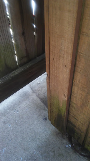 A close-up view of a wooden fence corner with some moss growing at the base.