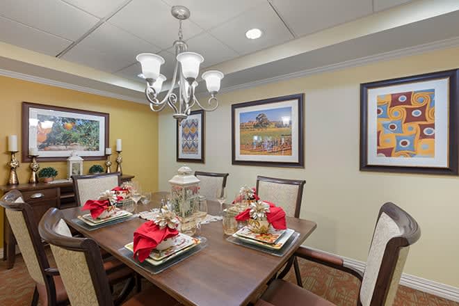 A beautifully set dining room table adorned with red napkins and surrounded by elegant decor, lit by a chandelier.