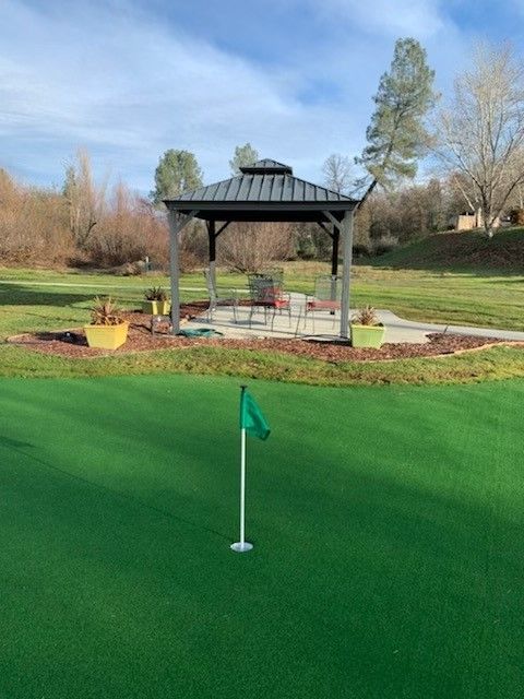 A serene outdoor setting featuring a putting green with a flag and a gazebo in the background.