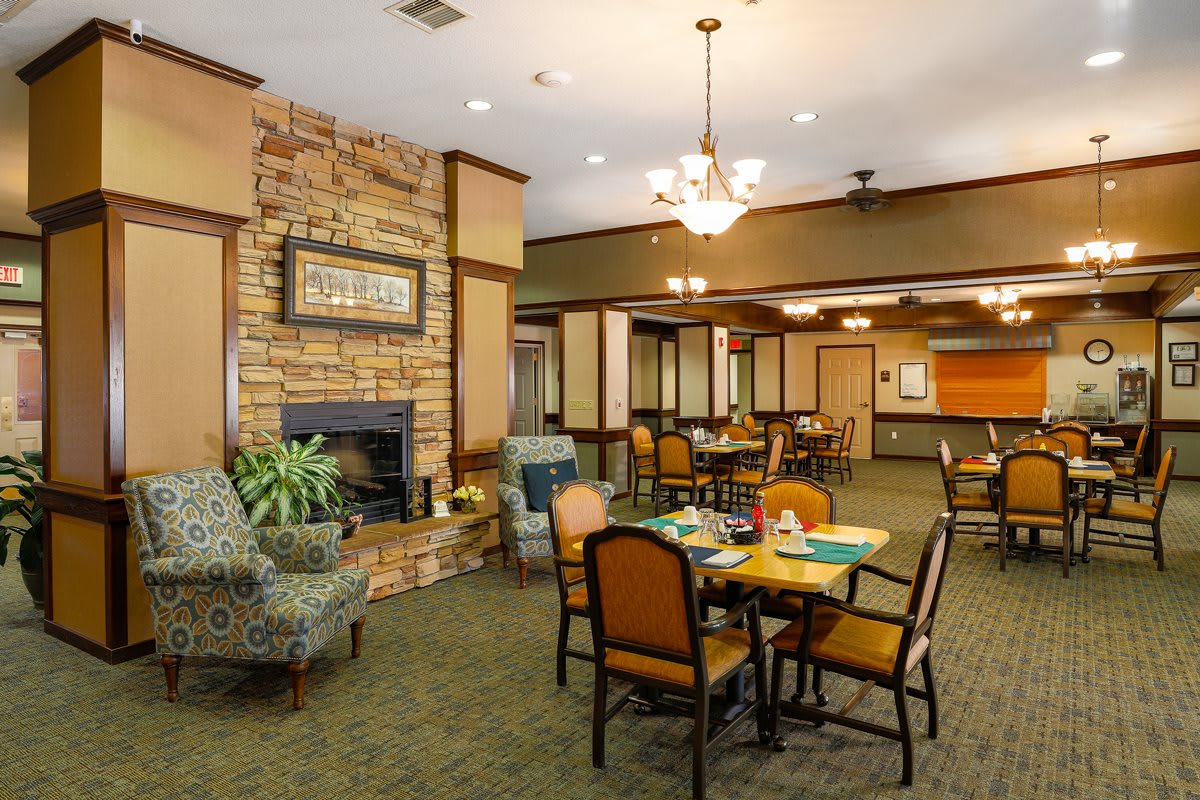 A cozy dining area with a fireplace, featuring tables and chairs under warm lighting.