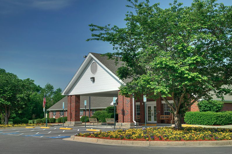 A brick building with a sloped roof surrounded by trees and a landscaped parking lot.