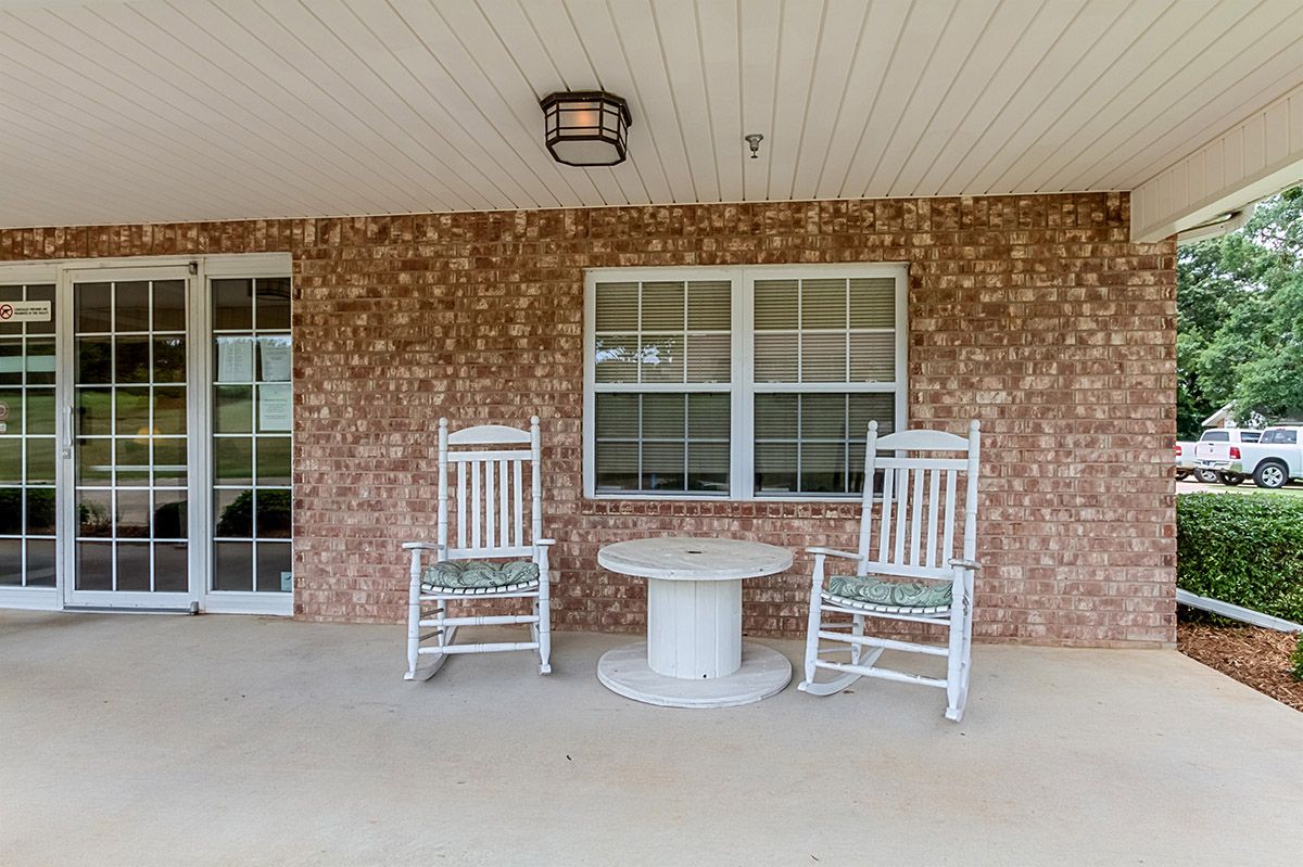 A cozy porch with two white rocking chairs and a small table against a brick wall.