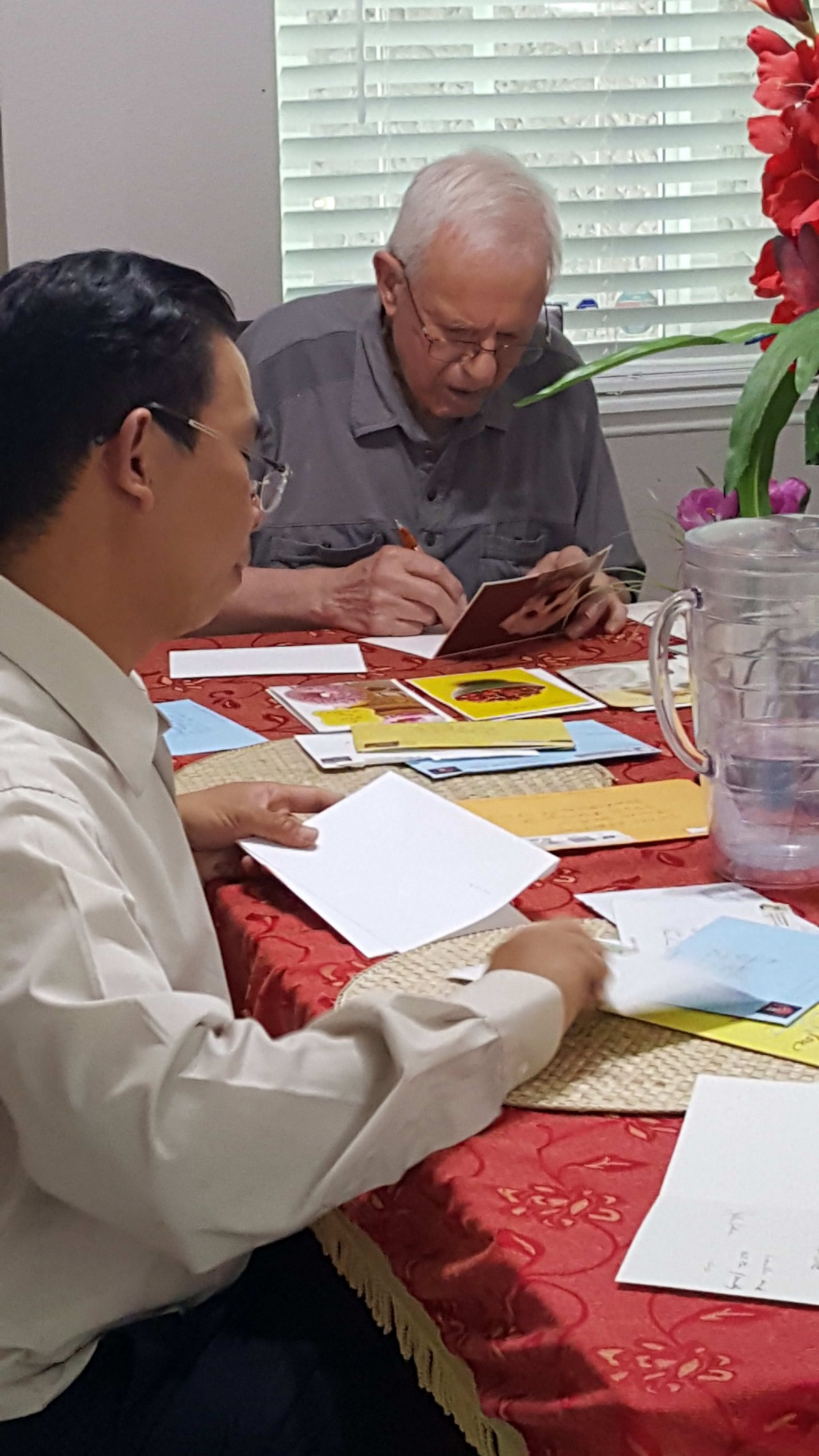 Two people sitting at a table, writing on cards.
