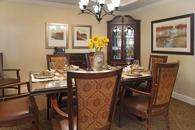 A well-decorated dining room with a central table set, chairs, and a chandelier overhead.