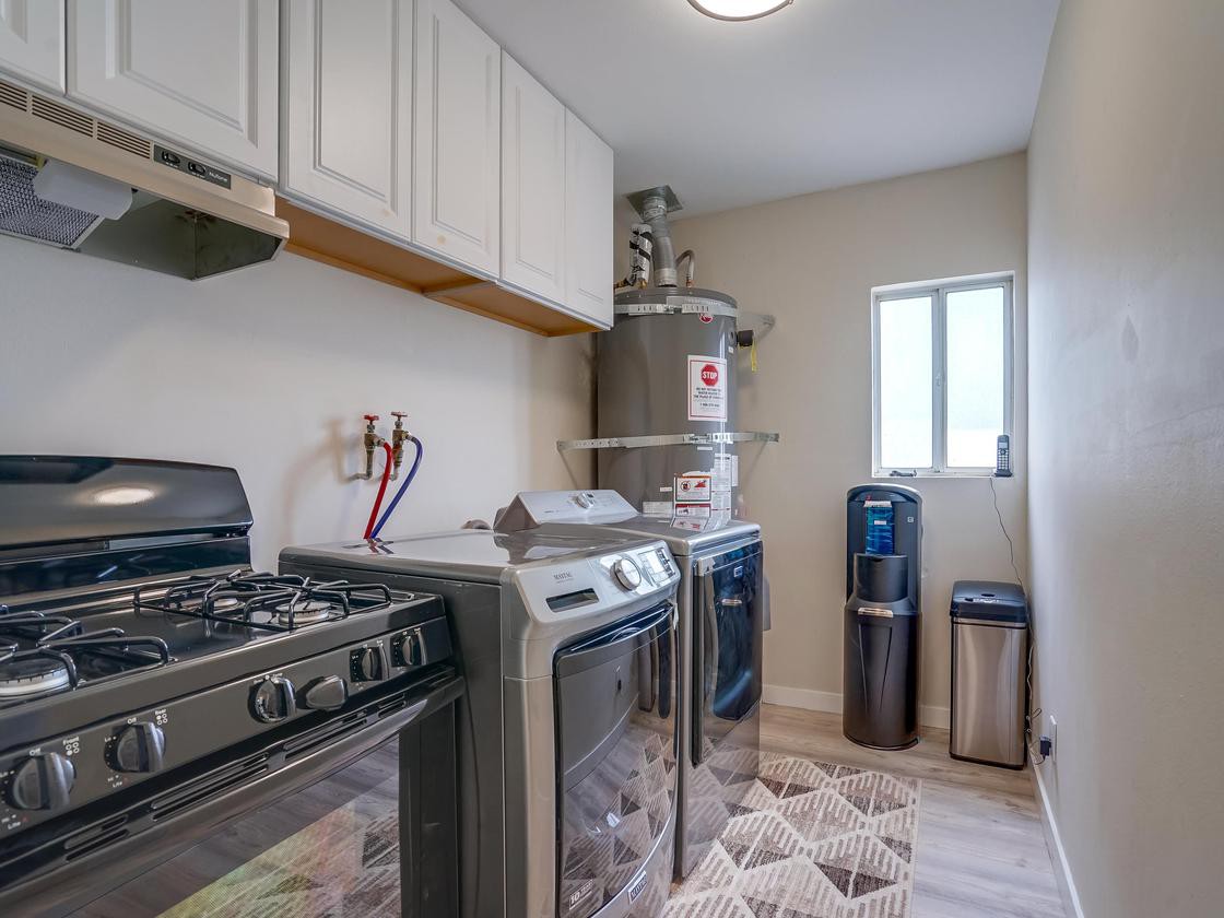 A well-organized laundry and utility room featuring a washing machine, dryer, water heater, and other appliances.