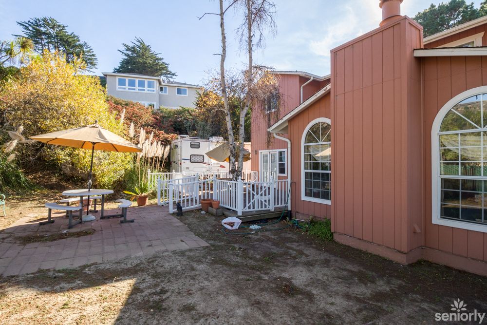 A cozy outdoor patio area with seating, surrounded by trees and a house with large windows.