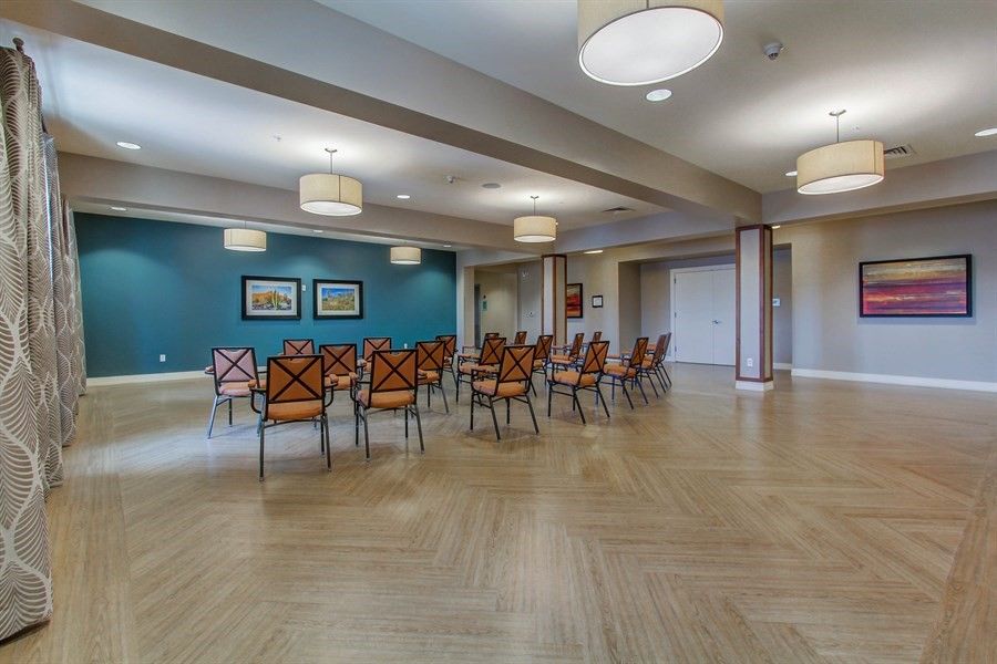 A spacious conference room with arranged chairs and tables, featuring a wooden floor and modern lighting.