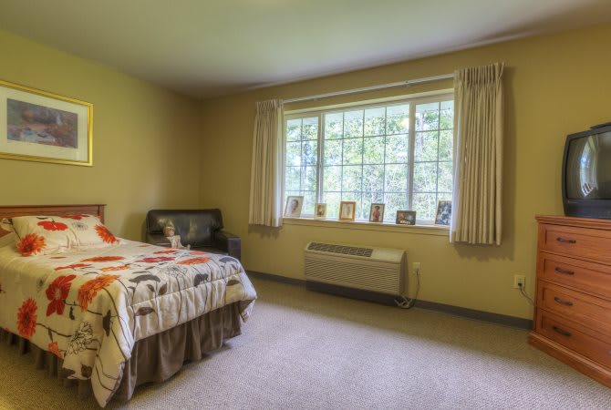 A cozy bedroom with a large window letting in natural light, featuring a bed and simple furnishings.