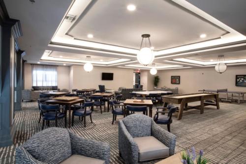 A spacious and modern lounge area with tables and chairs, featuring elegant lighting and a carpeted floor.