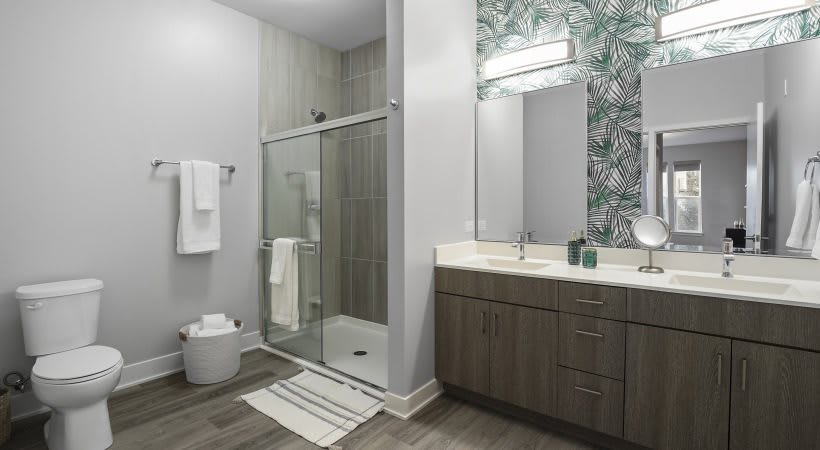A modern bathroom with a glass shower, vanity sink, and decorative wallpaper.