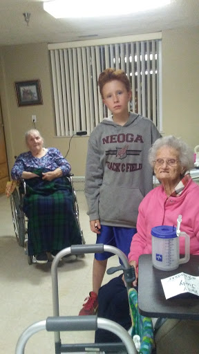 A young boy standing with two elderly women in a care home setting, highlighting moments of companionship.