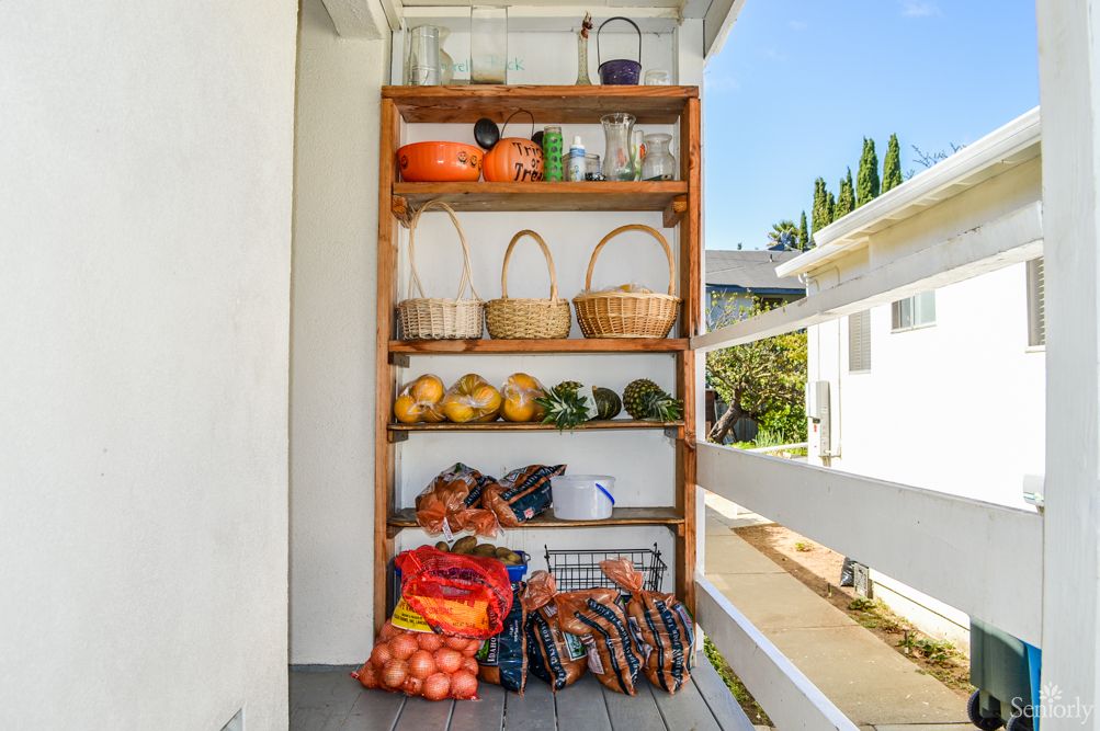A wooden outdoor shelf stocked with fresh fruits, vegetables, baskets, and jars.