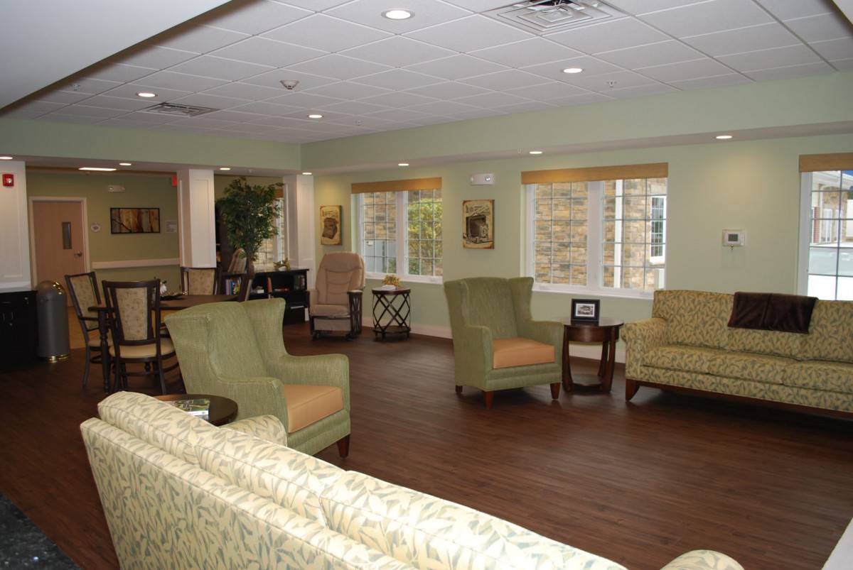 A cozy living room setup with sofas and chairs around tables, featuring large windows and wooden flooring.