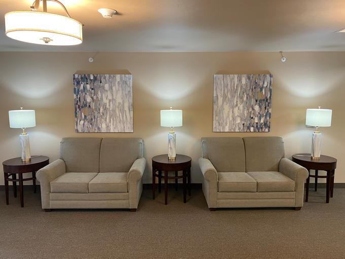 A cozy living room with two beige sofas, a lamp on a central table, and abstract art on the walls.