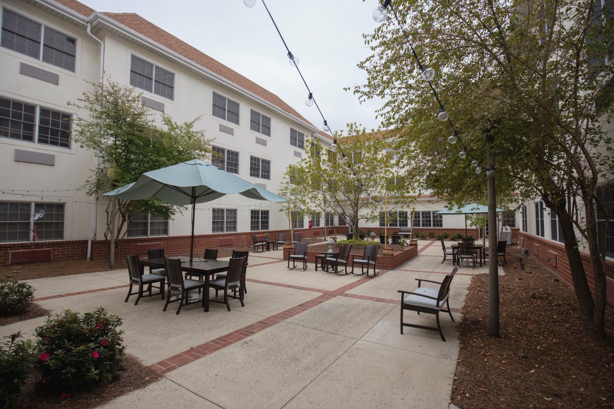 A courtyard with tables, chairs, and umbrellas next to a three-story building.