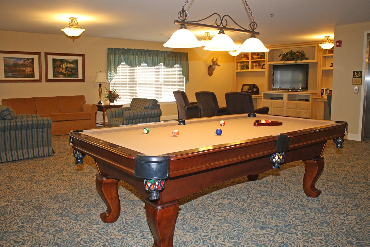 A cozy game room featuring a billiard table, comfortable seating, and warm lighting.