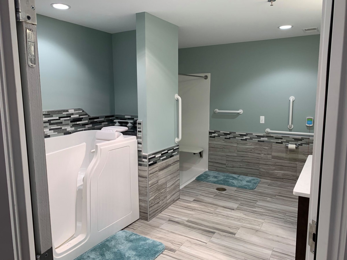 A modern, accessible bathroom with a walk-in tub and shower, featuring tile flooring and grab bars.