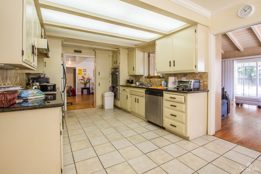 A modern kitchen with tiled flooring, cabinetry, and stainless steel appliances.