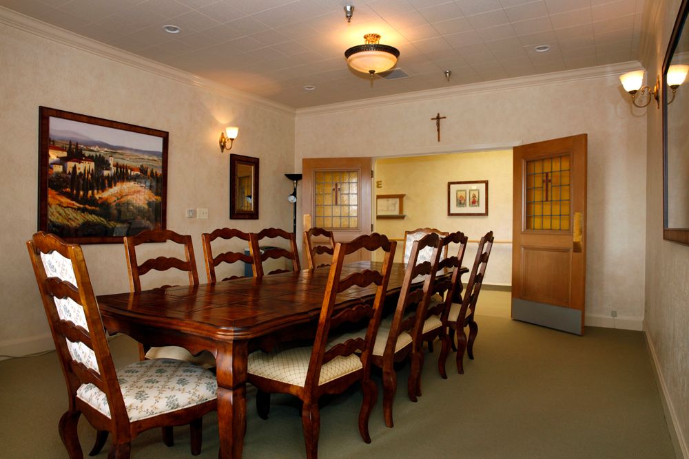 A formal dining room with a large wooden table and chairs, decorated with framed artwork and a ceiling light.