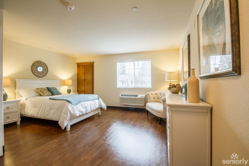 A cozy bedroom with a neatly made bed, wooden flooring, and soft lighting.