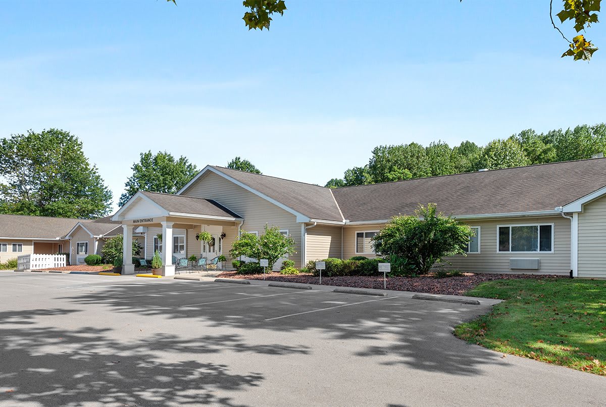 A single-story building with a driveway and surrounding greenery under a clear blue sky.