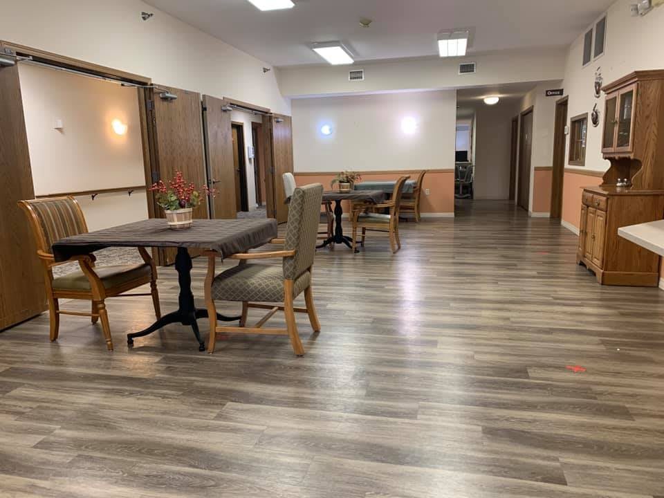 A spacious dining area with wooden flooring, featuring several tables and chairs under bright lighting.