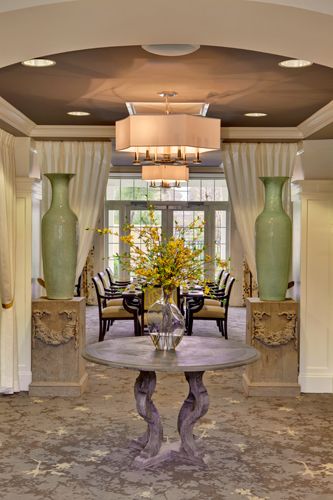 Elegant hallway leading to a dining area, featuring large vases and a central table with floral arrangement.