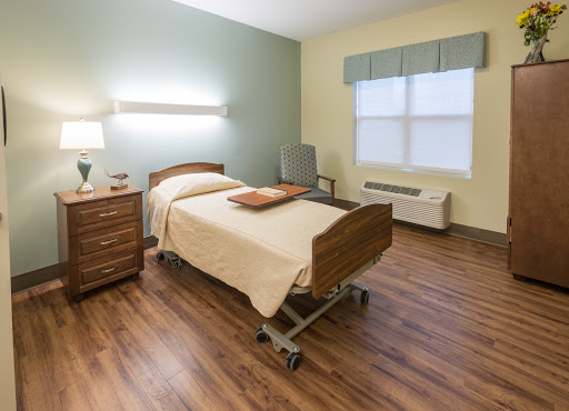 A well-lit hospital room featuring a neatly made bed, bedside table, and a large window.