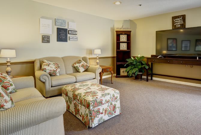 A cozy living room with a sofa, armchair, television, and floral ottoman.