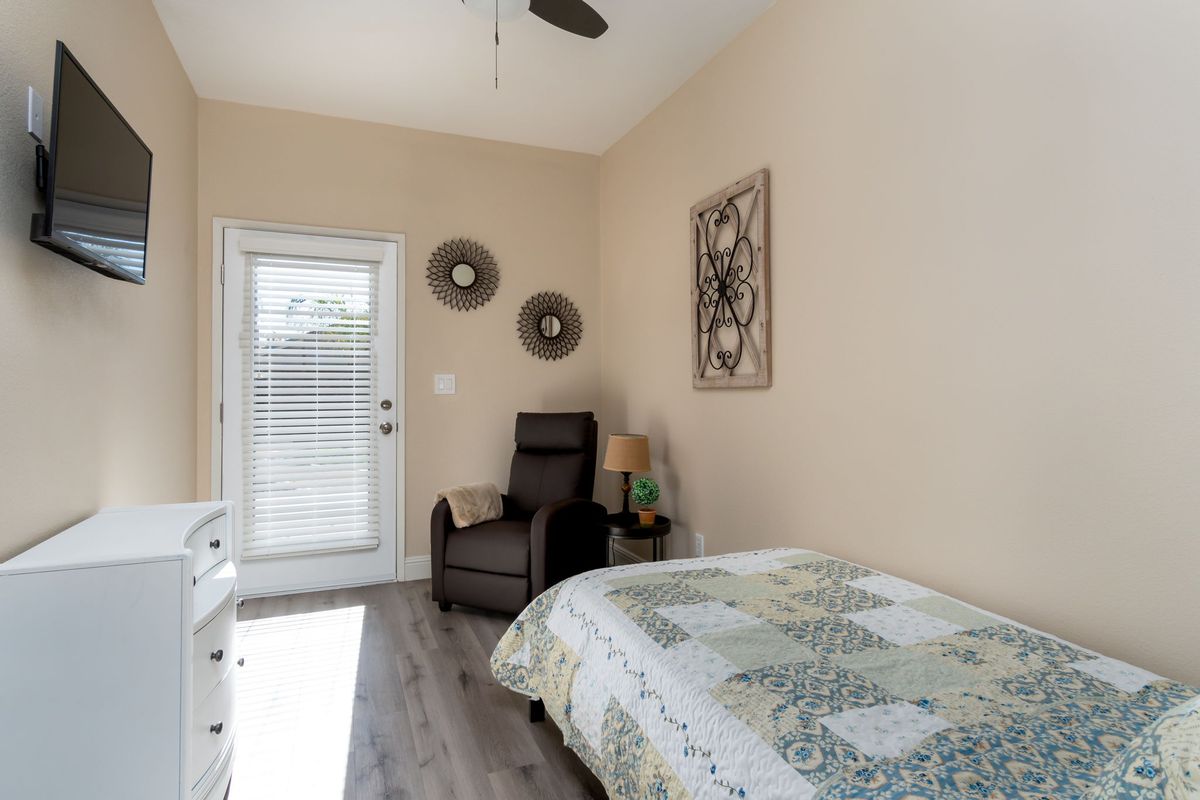 A minimalist bedroom featuring a bed with a patterned quilt, an armchair, wall decor, and abundant natural light.