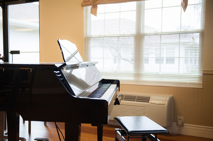 A sunlit room with a grand piano and stool by the window.