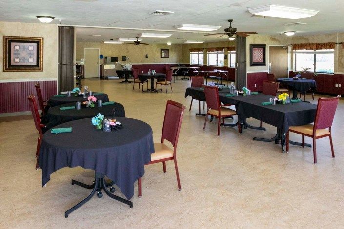 An empty event space with tables and chairs set up, featuring simple decorations.