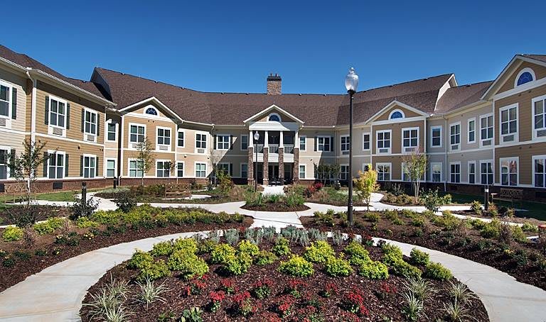 A large, beautifully landscaped residential building under a clear blue sky.