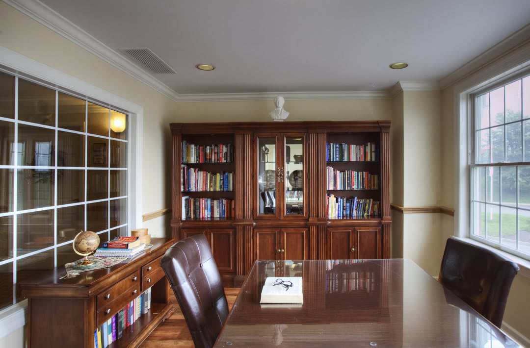 A well-furnished office space featuring wooden bookshelves filled with books, a desk, and a leather chair.
