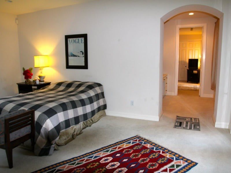 A cozy bedroom interior with a plaid bedspread and colorful rugs.
