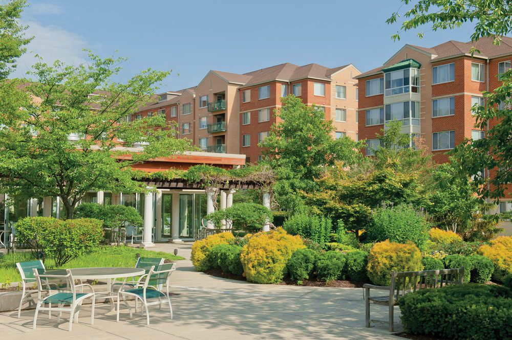 A well-maintained garden and patio area in front of a modern apartment building on a sunny day.