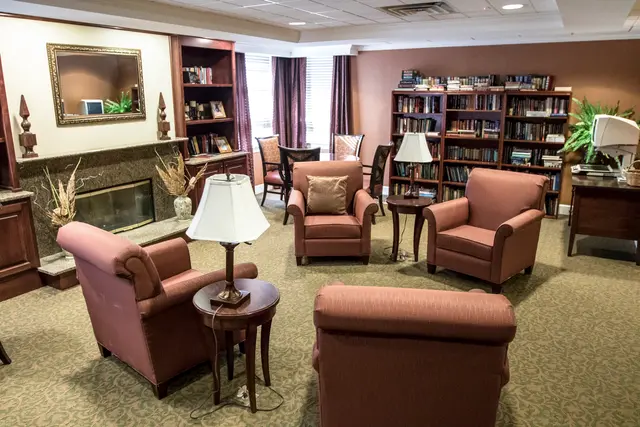 A cozy library seating area with armchairs, lamps, and bookshelves.